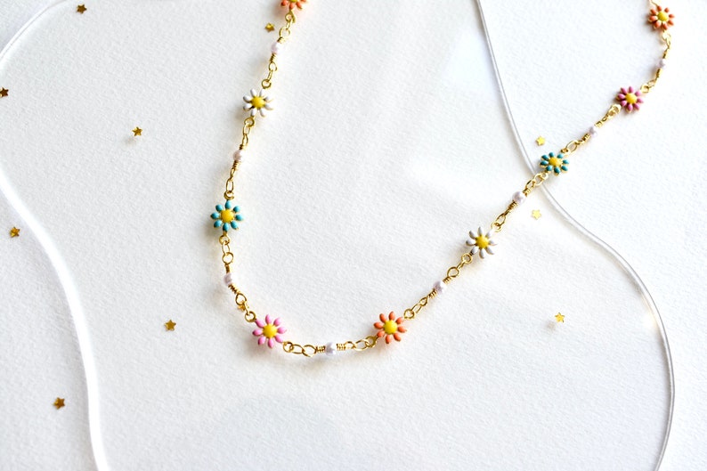 May include: A gold chain necklace with colorful flower charms. The flowers are pink, blue, yellow, and white.