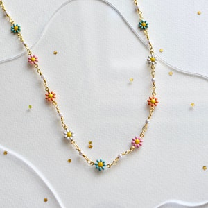 May include: A gold chain necklace with colorful flower charms. The necklace is on a white background with gold glitter.