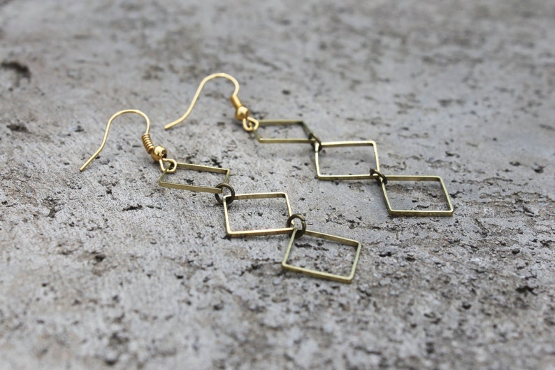 May include: Gold tone dangle earrings with a chain of connected square shapes.