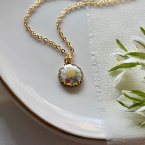 May include: A gold chain necklace with a round pendant featuring a white porcelain cameo with a yellow flower and red berries.