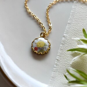 May include: A gold chain necklace with a white porcelain pendant featuring a floral design. The pendant has a scalloped edge and is accented with gold.