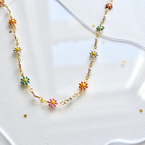 May include: A gold chain necklace with colorful flower charms. The flowers are pink, blue, green, and white with yellow centers.