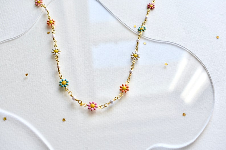 May include: A gold chain necklace with colorful flower charms. The flowers are pink, blue, green, and white with yellow centers.