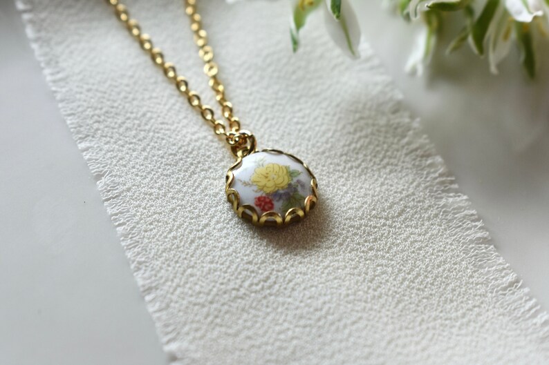 May include: A gold chain necklace with a round pendant featuring a floral design in shades of yellow, red, and green. The pendant is surrounded by a gold filigree frame.
