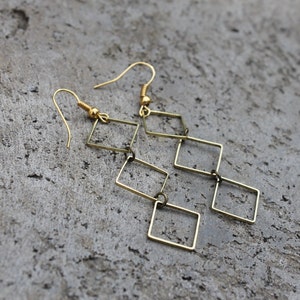 May include: Gold-toned dangle earrings with a geometric design featuring multiple connected square shapes.