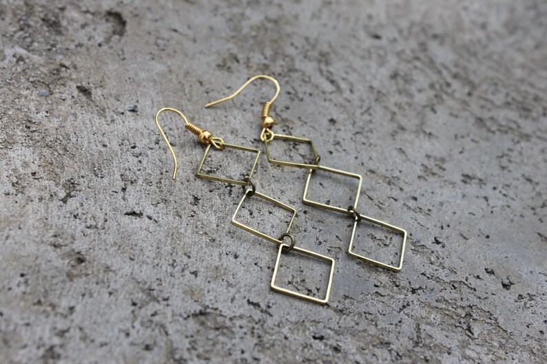 May include: Gold-toned dangle earrings with a geometric design featuring multiple connected square shapes.