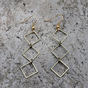 May include: Gold-toned dangle earrings with a chain of four connected square shapes.