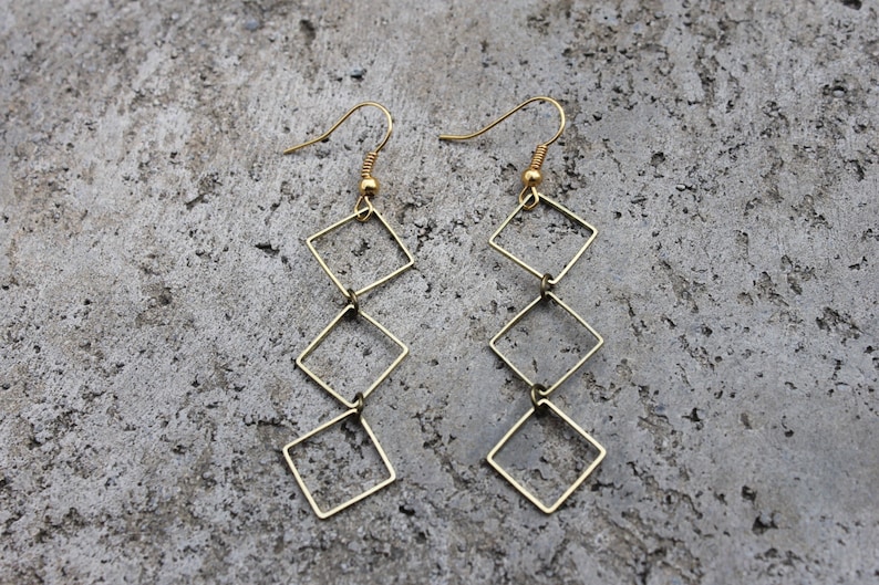 May include: Gold-toned dangle earrings with a chain of four connected square shapes.