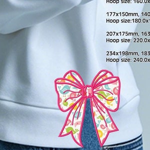 May include: A colorful embroidered bow with pink, blue, and yellow birds on a white background. The bow is on a light blue sweatshirt. The text "Original Design by Cherrystitchdesign" and "CherryStitch" is at the bottom of the image.
