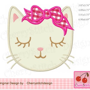 May include: White cat face with closed eyes and a pink and red gingham bow. The cat face is embroidered and has a pink nose and brown whiskers.
