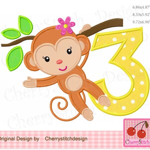 May include: A brown monkey with a pink flower in its hair is holding onto a branch and a yellow number 3 with white polka dots. The number is 9.72 inches wide and 6.90 inches tall.