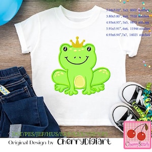 Peut inclure: Un t-shirt blanc avec une grenouille verte portant une couronne dorée brodée sur le devant. La grenouille sourit et a un ventre jaune. Le t-shirt est sur une surface en bois avec un jean bleu et une paire de baskets noires.