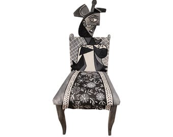 Könnte beinhalten: Ein schwarz-weißer Stuhl mit einem floral gemusterten Sitz und einer kubistischen Figur, die auf die Rückenlehne gemalt ist.