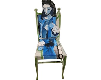 Könnte beinhalten: Ein bemalter Stuhl mit einer Frau in Blau und Weiß. Die Stuhllehne und die Beine sind grün. Der Sitz zeigt eine schwarze Katze. Das Kunstwerk erinnert an den Stil von Picasso.
