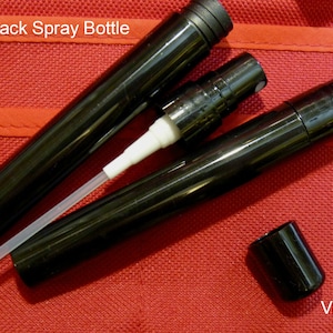 May include: Three black 10ml spray bottles with a white nozzle. The bottles are on a red fabric background.