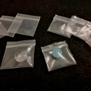 May include: A collection of clear plastic resealable bags with a blue pill and a clear object inside one of the bags.