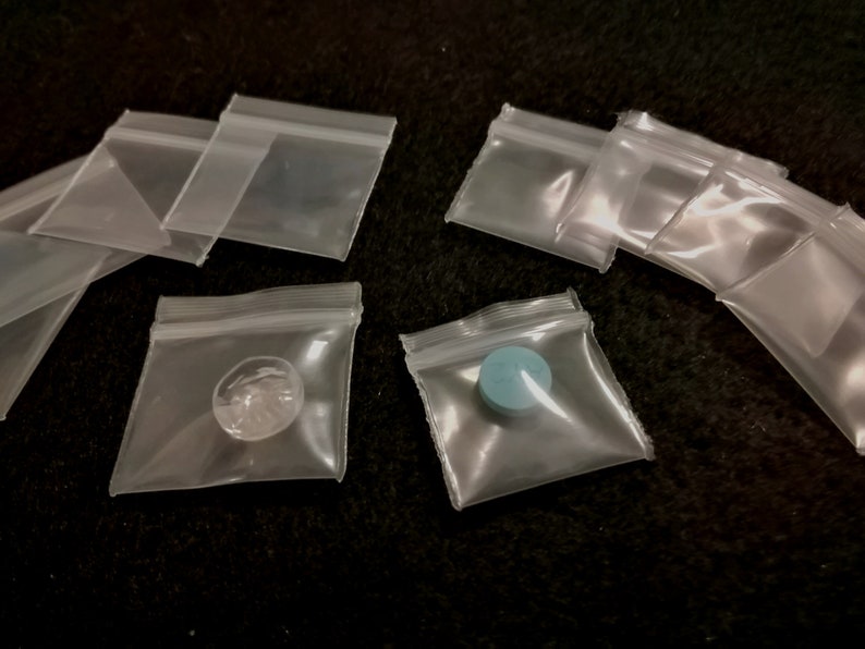 May include: A collection of clear plastic resealable bags with a blue pill and a clear object inside one of the bags.