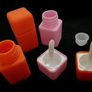 Könnte beinhalten: Vier kleine quadratische Behälter mit Applikatoren. Zwei Behälter sind orange und zwei sind rosa. Die Behälter sind aus Kunststoff und haben einen Schraubverschluss. Die Applikatoren sind weiß und haben eine Bürstenspitze.