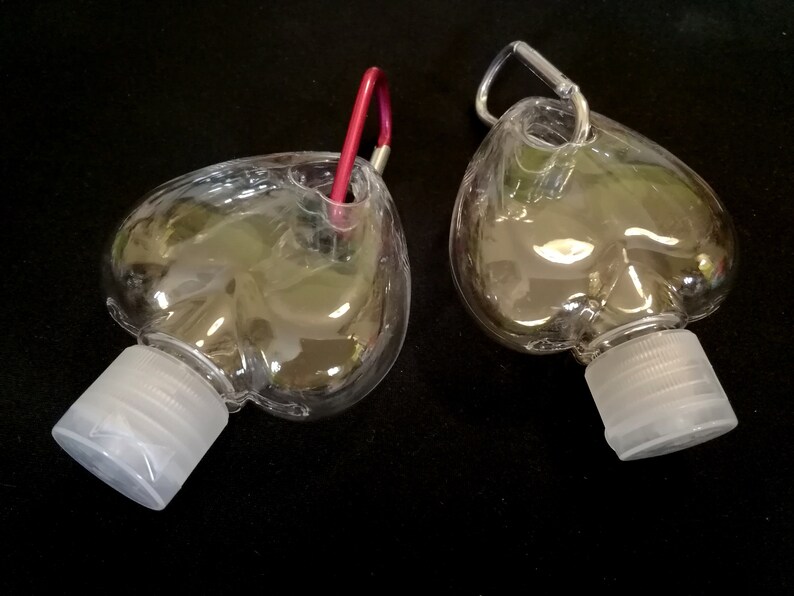 May include: Two clear plastic heart-shaped bottles with silver carabiner clips. The bottles have white screw-on caps.