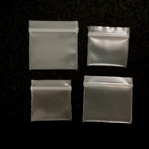 May include: Four clear plastic zippered bags of various sizes. The bags are on a black background.