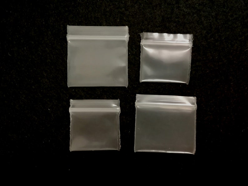 May include: Four clear plastic zippered bags of various sizes. The bags are on a black background.