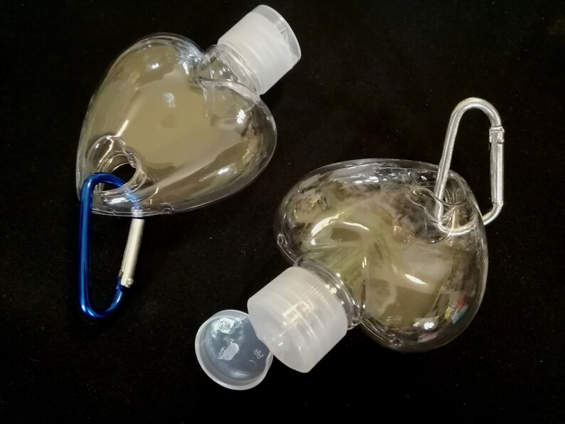 May include: Two clear plastic heart-shaped bottles with white screw-on caps and a silver carabiner clip attached to one bottle.