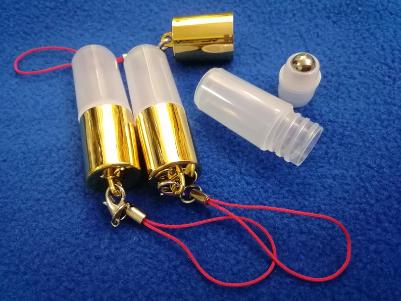 Op de afbeelding: Twee transparante glazen rollerflessen met gouden doppen en rode koordjes. Een derde transparante glazen rollerfles met een zilveren rolbal is ook te zien.