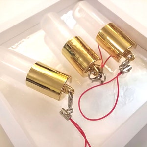 Op de afbeelding: Drie transparante glazen flessen met gouden doppen en een rood touwtje eraan vastgemaakt. De flessen bevinden zich in een witte doos.