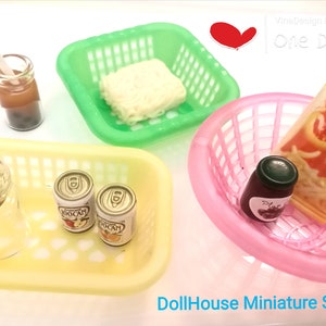 May include: Dollhouse miniature set with a variety of items, including a green basket with a block of white noodles, a yellow basket with two cans of soda, a pink basket with a jar of jam and a package of shrimp crackers, and a clear glass jar with a cork stopper.