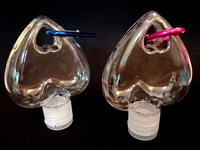 May include: Two clear plastic heart-shaped bottles with a small loop at the top. The bottles have white screw-on caps. One bottle has a blue loop and the other has a pink loop.