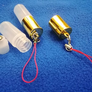 Op de afbeelding: Twee transparante glazen rollerflessen met gouden doppen en een rood koord. E&eacute;n fles heeft een zilveren rollerbal en de andere een gouden dop.