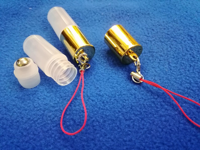 Op de afbeelding: Twee transparante glazen rollerflessen met gouden doppen en een rood koord. E&eacute;n fles heeft een zilveren rollerbal en de andere een gouden dop.
