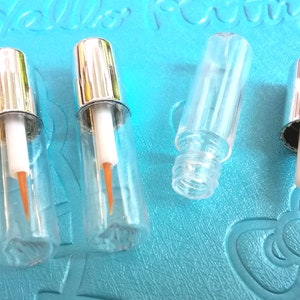 May include: Five clear glass bottles with silver caps and a thin orange applicator tip. The bottles are on a blue textured surface.