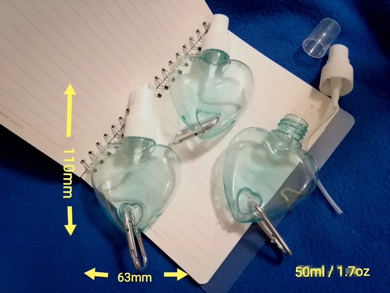 May include: Three heart-shaped, clear blue spray bottles with white spray nozzles and silver carabiner clips. Each bottle is approximately 4.3 inches tall and 2.5 inches wide, with a capacity of 1.7 ounces.