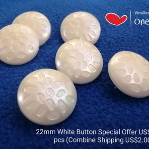 Puede incluir: Cuatro botones de plástico blanco con un diseño floral en relieve. Los botones tienen un diámetro de 22 mm.