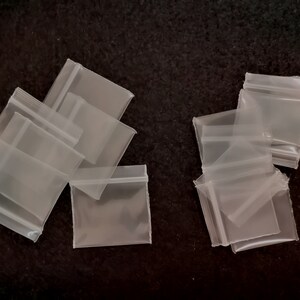 May include: A group of clear plastic resealable bags with a zipper closure. The bags are arranged in two groups on a black surface.
