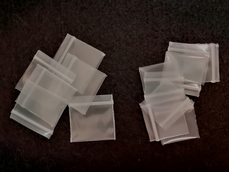 May include: A group of clear plastic resealable bags with a zipper closure. The bags are arranged in two groups on a black surface.