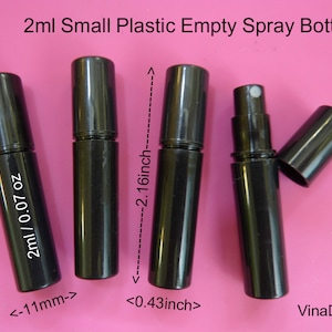 Puede incluir: Cuatro botellas de spray vacías de plástico negro de 2 ml con un atomizador plateado. Las botellas miden 5,5 cm de alto y 1,1 cm de ancho. Las botellas están sobre un fondo rosa.