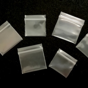 May include: Six clear plastic zippered bags of various sizes on a black background.