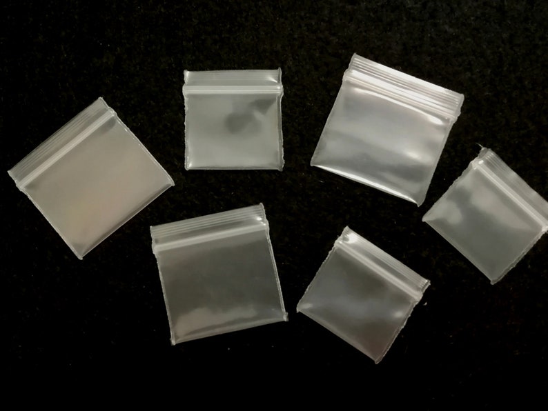May include: Six clear plastic zippered bags of various sizes on a black background.