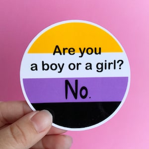 May include: A round sticker with the non-binary pride flag colors: yellow, white, purple, and black. The text reads, "Are you a boy or a girl? No."