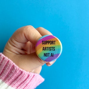 May include: A rainbow-colored button with the text "Support Artists Not AI" in black.