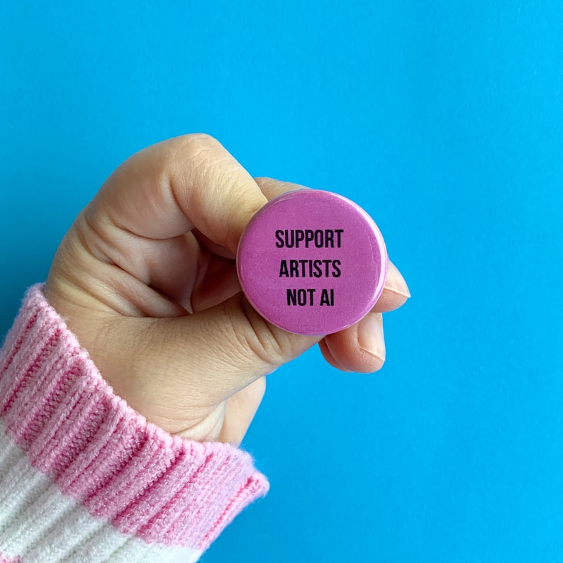 May include: A pink button with the text "SUPPORT ARTISTS NOT AI" in black lettering.