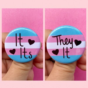 May include: Two round buttons with the transgender pride flag colors. The first button says "It Its" with a heart symbol. The second button says "They It" with a heart symbol.