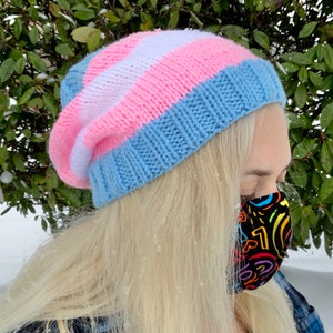 May include: A blue, pink and white striped knitted beanie with a black and white patterned face mask.