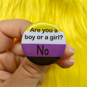 May include: A round button featuring the colours of the non-binary pride flag. The button displays the text "Are you a boy or a girl? No."