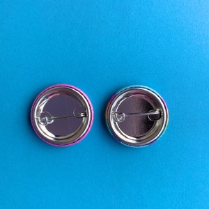 May include: Two round button pins with rainbow colored designs. The back of the pins are silver with a metal pin back.
