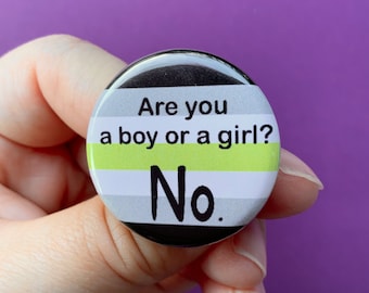 May include: A round button with a black border and a design featuring the text "Are you a boy or a girl? No." The background has horizontal stripes in white, gray, and a bright green color.