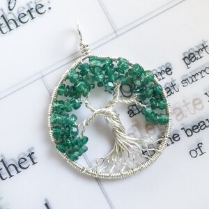 May include: A silver wire wrapped tree of life pendant with green gemstone leaves.