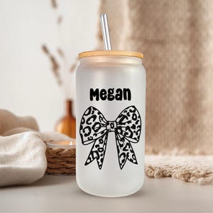 Pu&ograve; includere: Un bicchiere di vetro bianco smerigliato con un coperchio in bamb&ugrave; e un fiocco con stampa leopardata in bianco e nero. Sul bicchiere &egrave; scritto il nome "Megan".